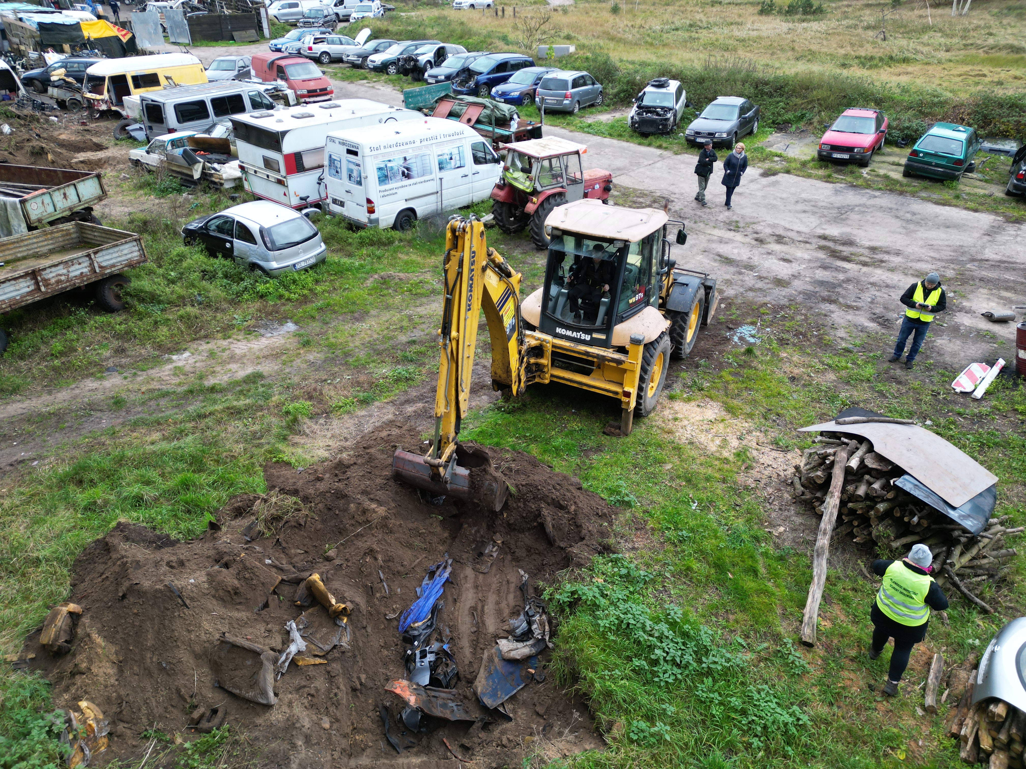 Prace koparki na tle zdemontowanych pojazdów